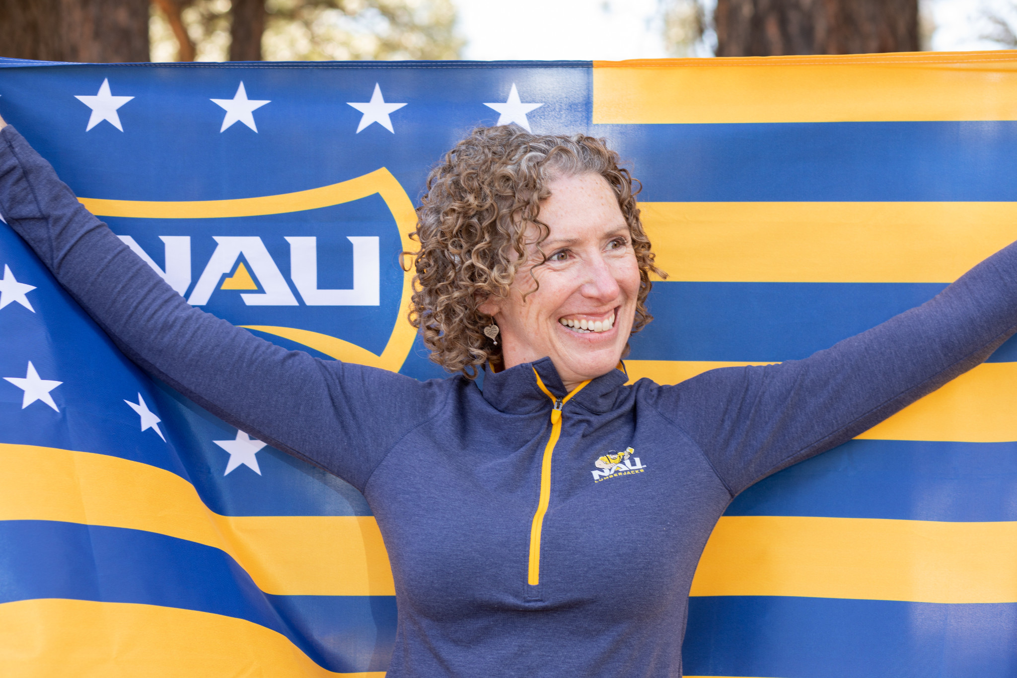 A person smiles while proudly holding an N A U flag and wearing N A U gear.