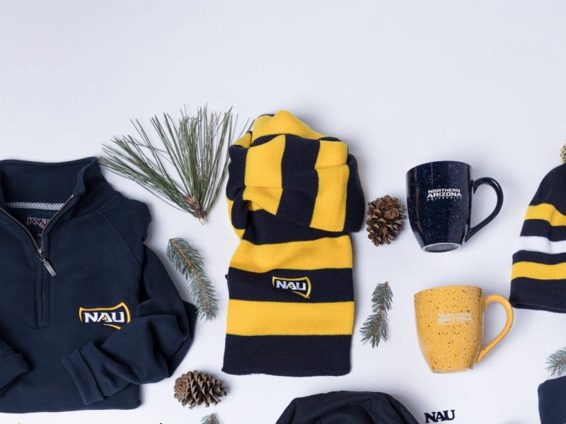 Various N A U logo-branded items: cozy quarter-zip, stylish scarf, and mugs.
