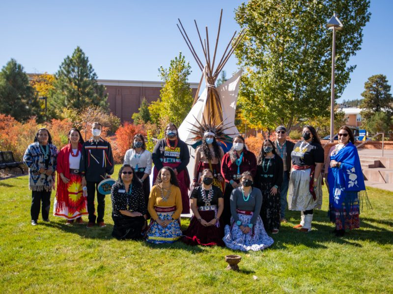 People standing in front of a teepee outside of the Native American Cultural Center the NACC