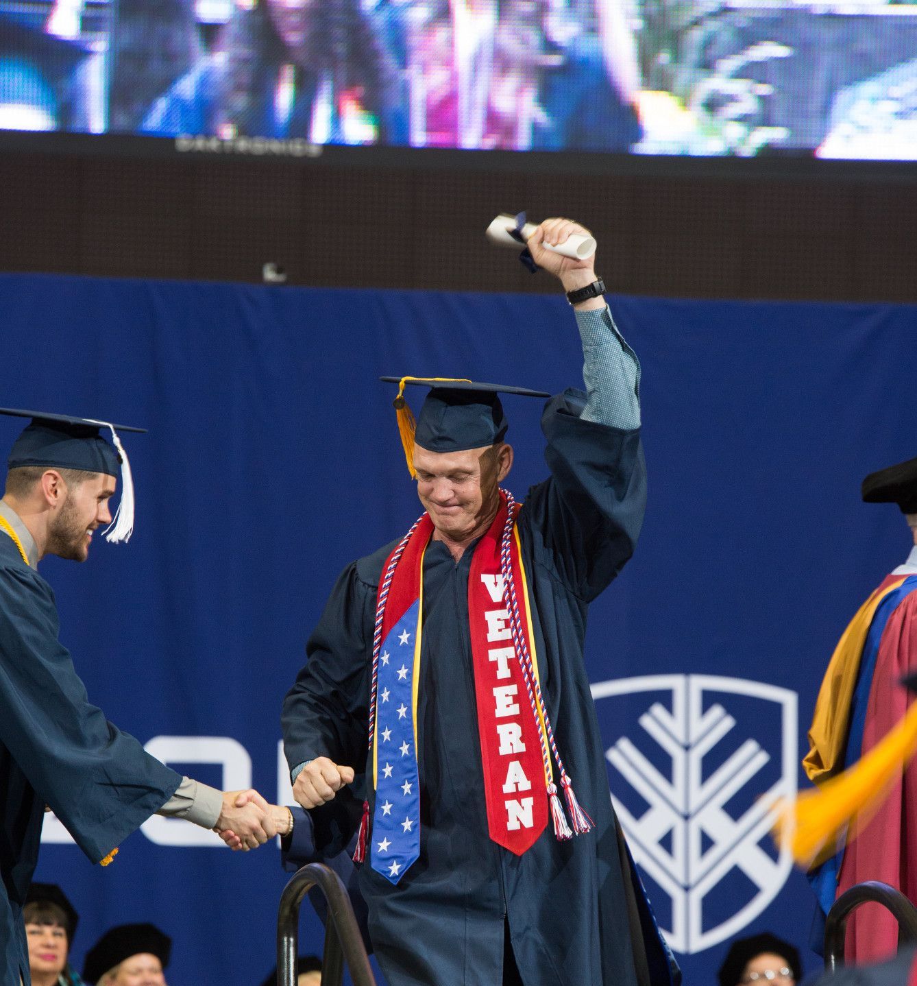 An NAU veteran graduates and holds his arm up in victory.