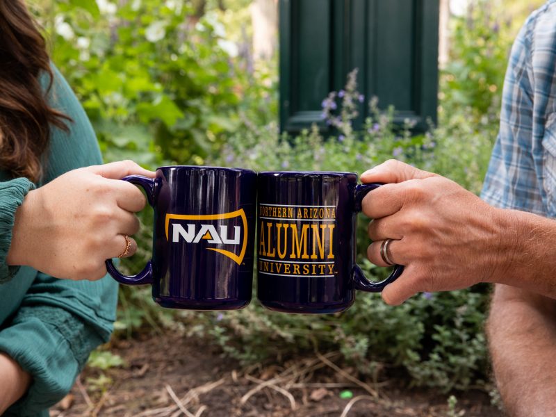 Two NAU alumni clinking coffee cups together.