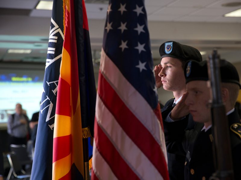 Military-affiliated students presenting flags in traditional military attire at a veterans' convocation event.