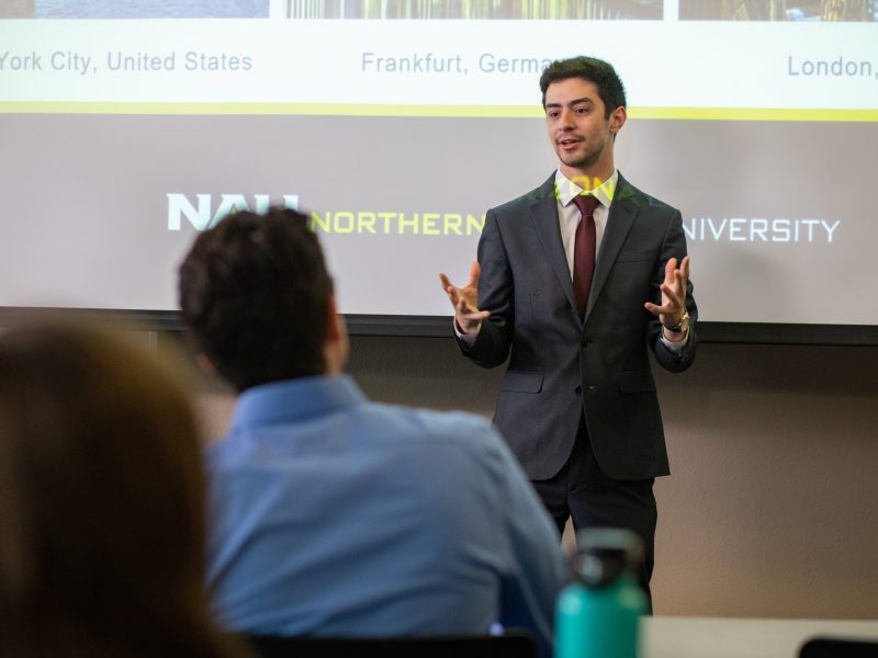 Student presenting in front of a projector screen that reads, 'Northern Arizona University'.
