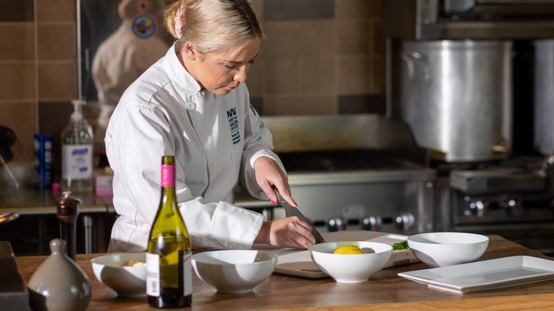 School of Hotel and Restaurant Management student slicing lemon in professional kitchen attire.