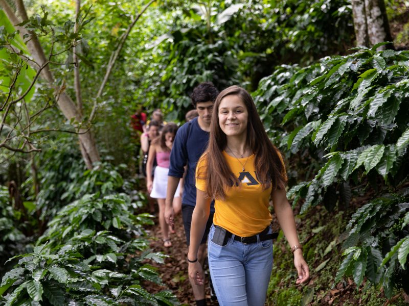 Smiling student hiking while wearing orange Northern Arizona University t-shirt with a line of other hikers behind.