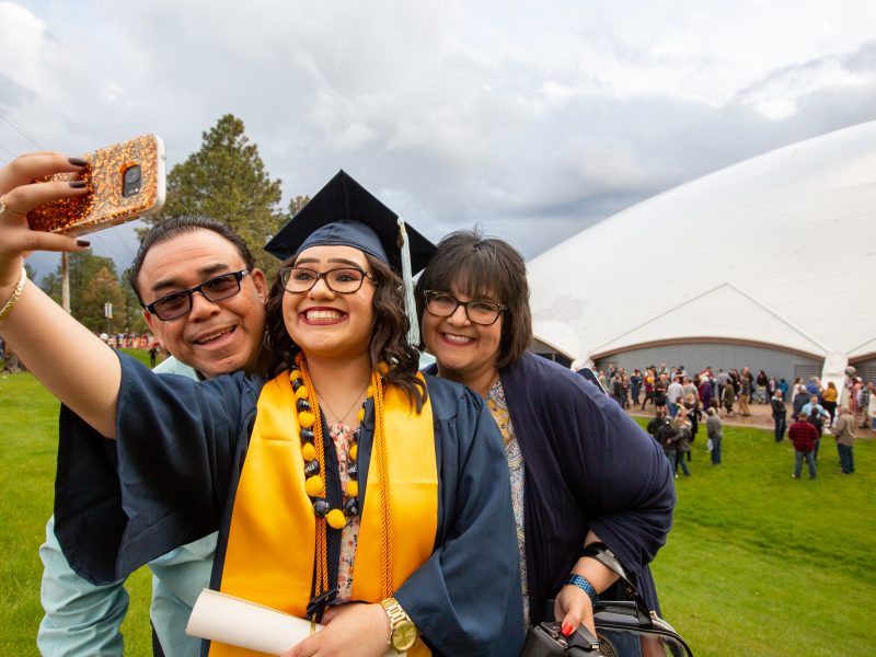 NAU graduate taking selfie in cap and gown outside commencement.