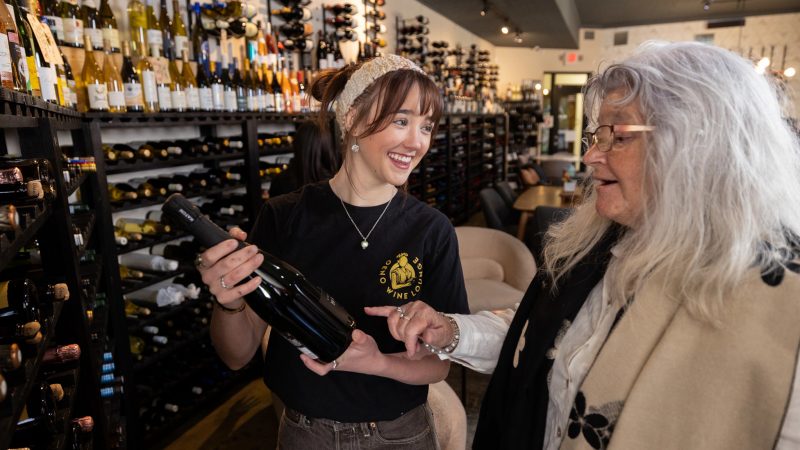 Student assisting customer with wine selection at local wine shop.