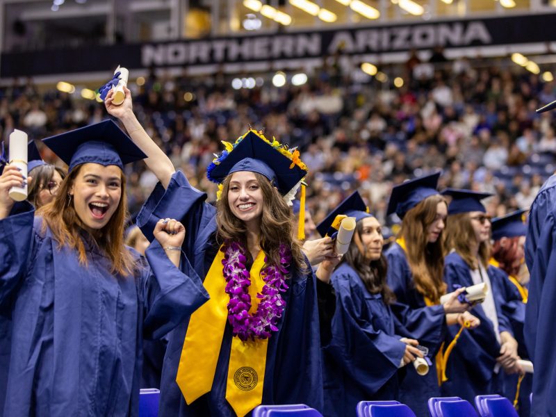 Two students graduating, one is holding up their arm in excitement.