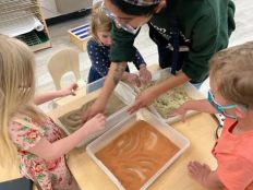 Teacher working with children and three binds of different types of sand.