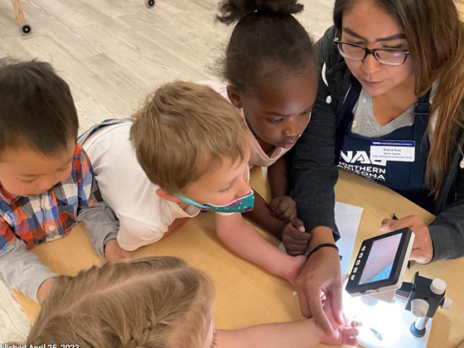 Teacher and four children looking through a digital microscope, holding rocks under the scope.