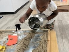 A child pouring water in a path of sand to make a trough.