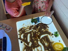 Two children standing at a light table with sand poured over it.
