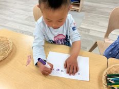 A child writing symbols and small scribbles on a paper with purple marker.