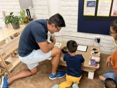 A child and his dad looking at an activity on a small table on the floor.