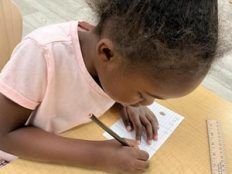 Child writing on a card with colored pencil.