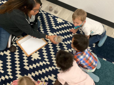 Teacher showing a jar of sand to several students sitting on a rug.