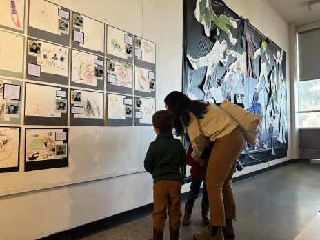A mom and child looking at a child' created art display that includes drawings and photos.
