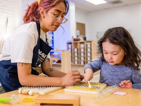 A teacher and child using geoboards and rubber bands to create a pattern at a table.