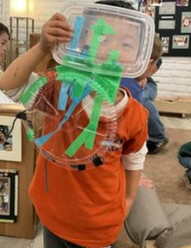 A child holding up recyclable materials attached with tape to make a spider.