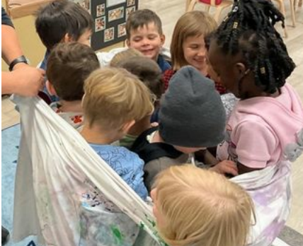 Children wrapped closely together in a sheet imitating a multi-person dress.