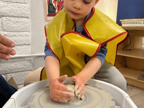 A child using his hands to mold clay at a pottery wheel.