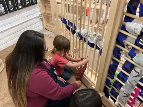 A teacher helping a child weave fabric on a large loom.