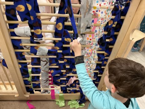 A child pulling on blue fabric in a classroom loom.