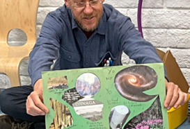 A teacher holding up a sample collage on green paper, including magazine cutouts.