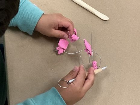 Hands twisting wire and clay.