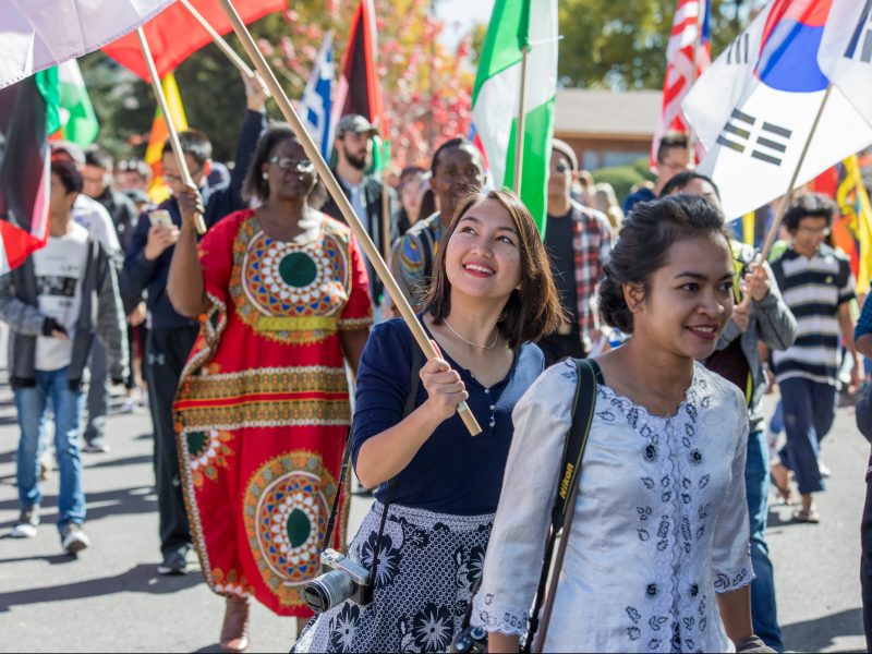 Students walk in a parade with international flags.