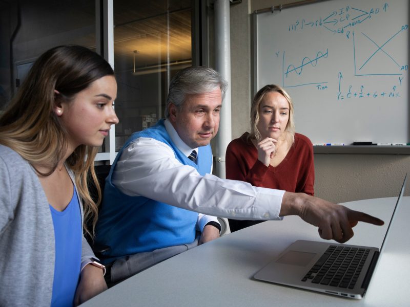 A professor helping two students with work on a lap top.