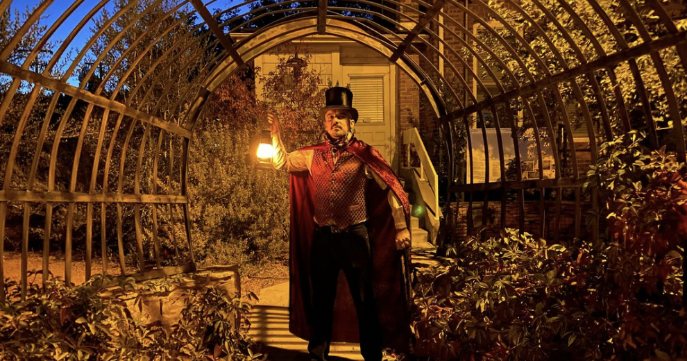 A man with a top hat and cape holding a lantern