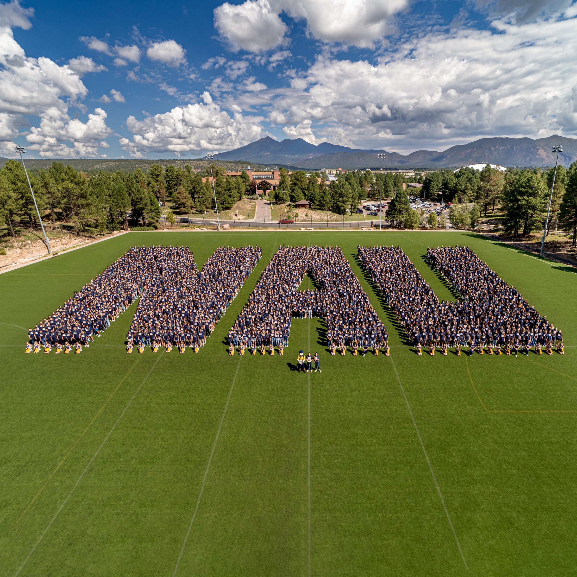 A group of people standing in a field spelling out NAU.