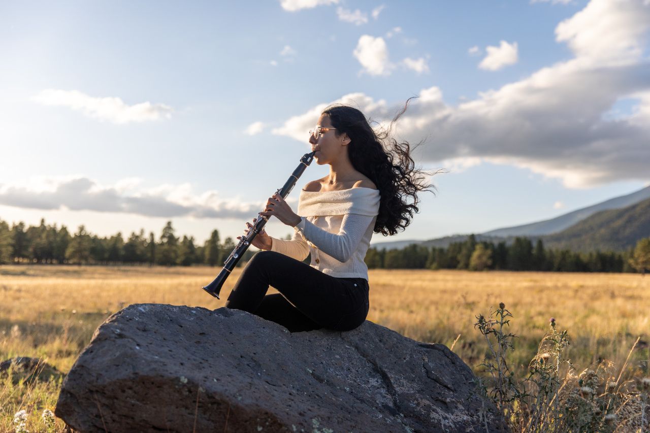 A woman sitting on a rock playing a wind instrument.