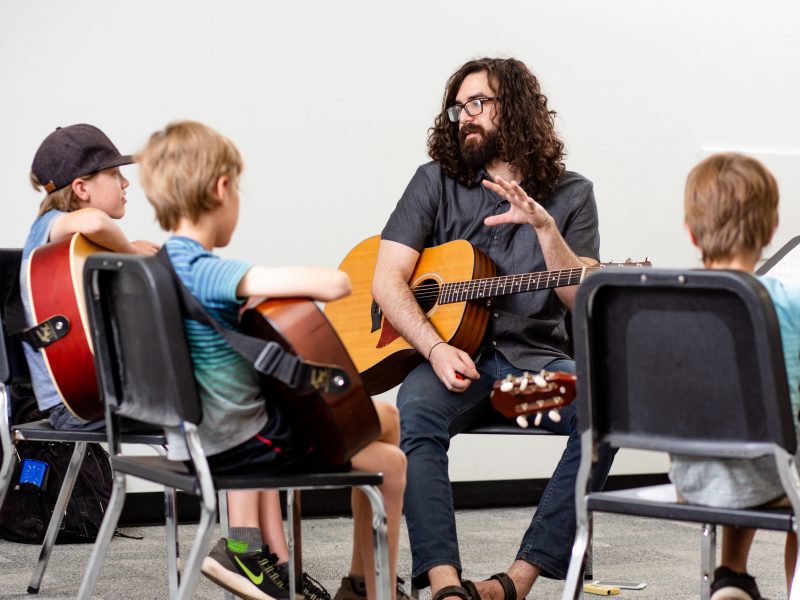 Children learning guitar from tutor.