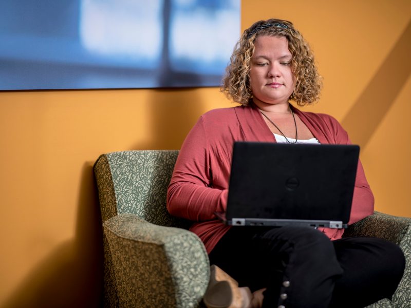 An NAU student sitting on a couch, looking at her laptop.