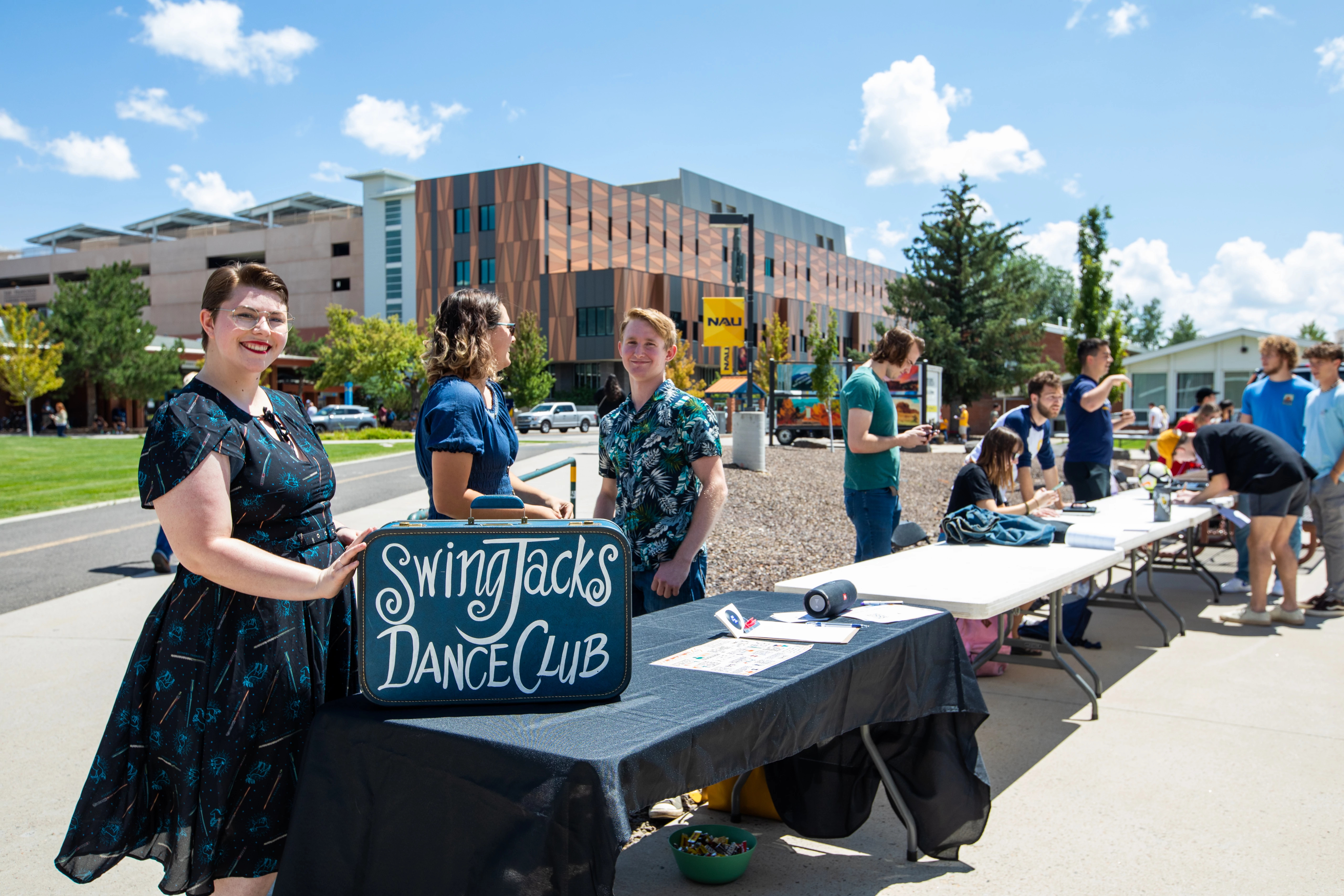 Students stand in front of Swing Jacks Dance Club table outside smiling.