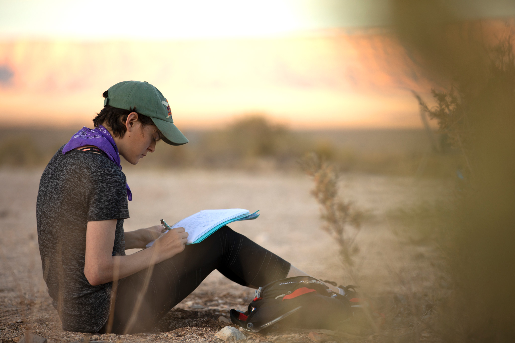 Student writes in a journal while sitting on the ground