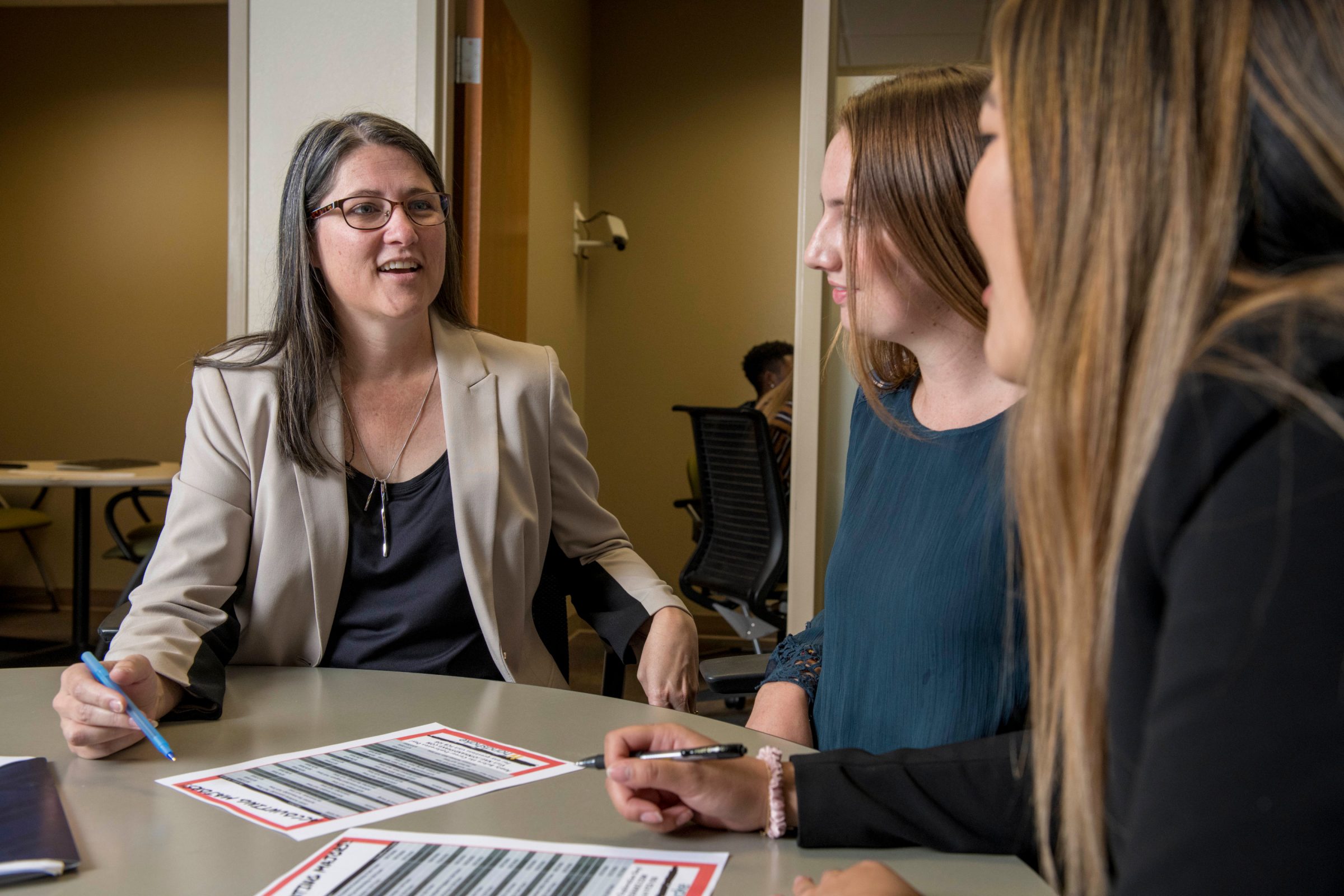 An academic advisor speaking with two students around a table.