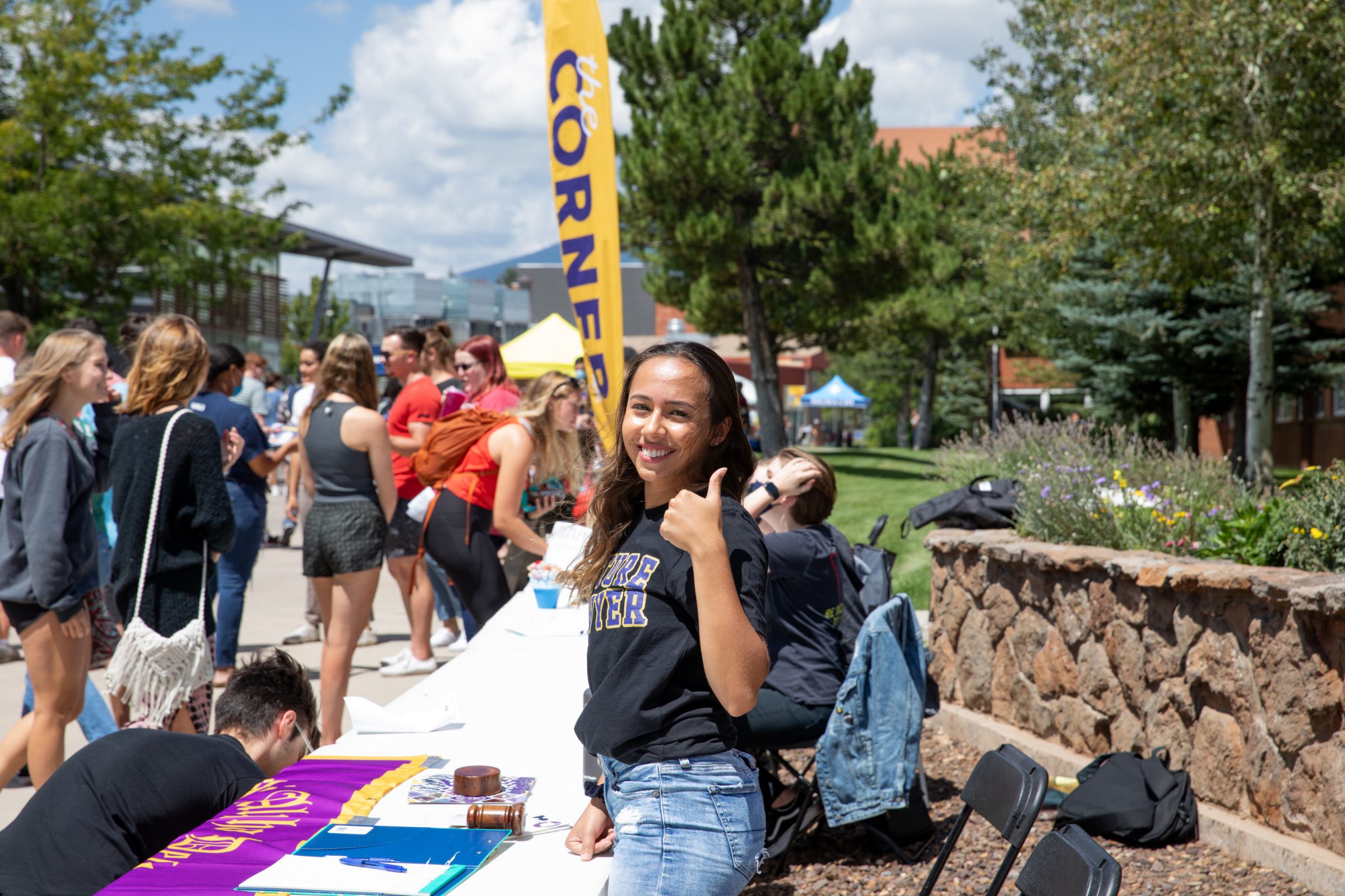 A student smiling and giving a "thumb's up" at a club booth outside.