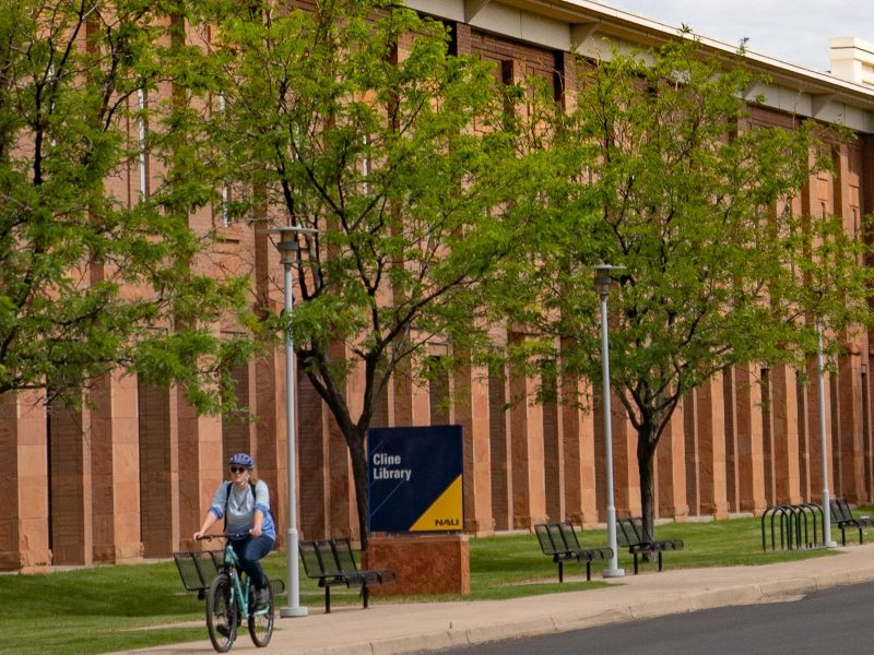 Exterior image of Cline Library at NAU with a student riding their bike.