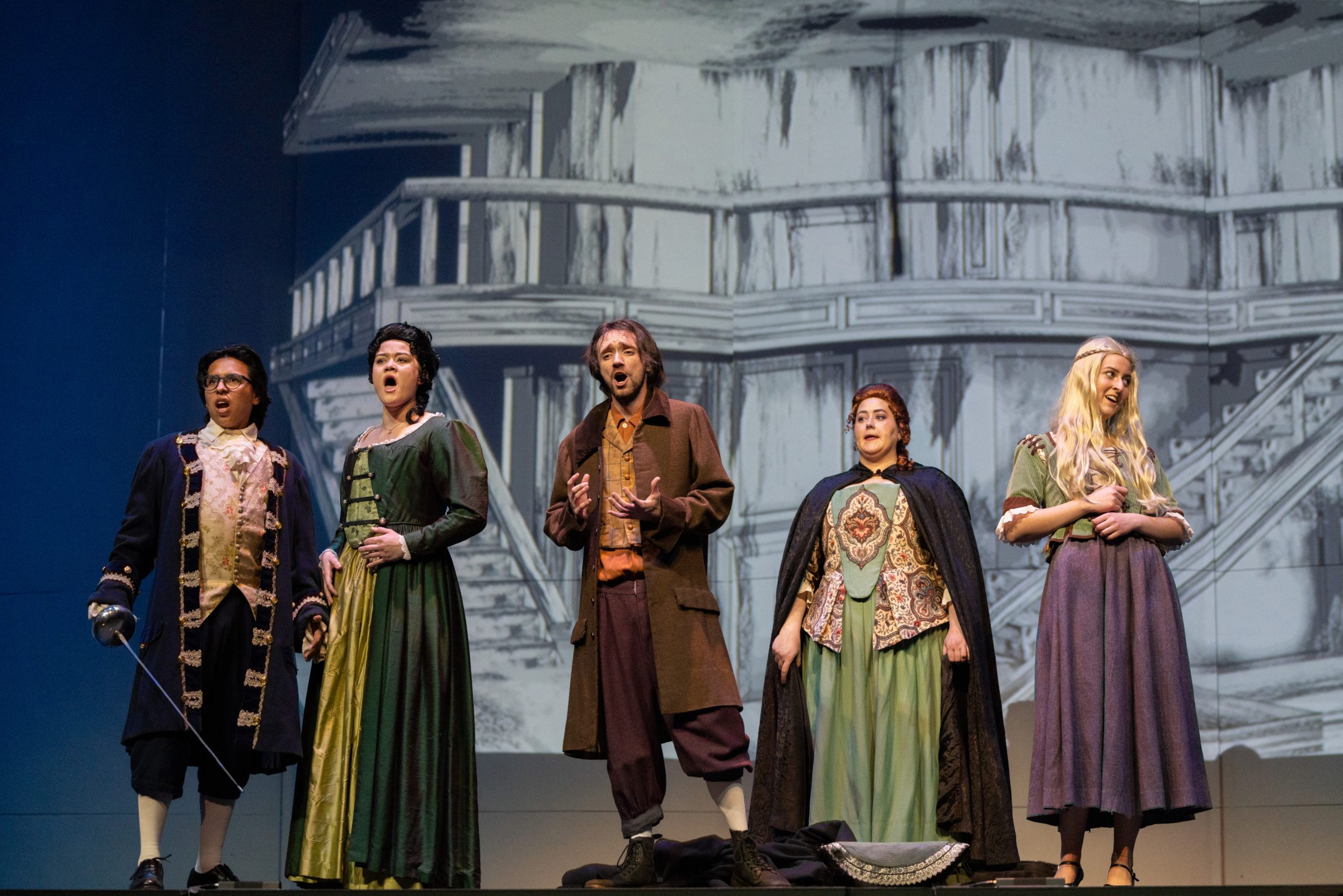 A group of opera performers dressed in character and singing on a stage.