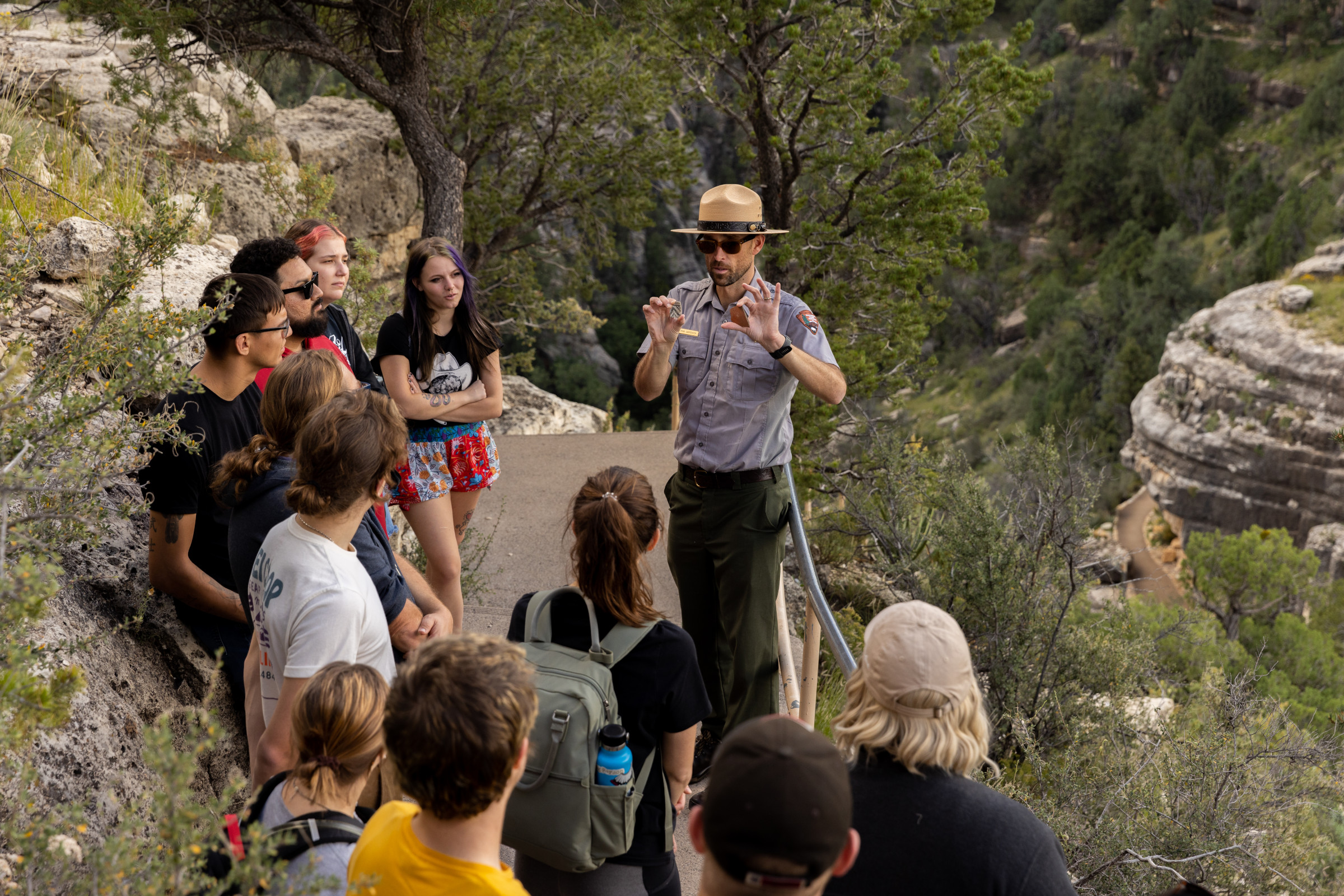 A group of students listening to a park ranger in the middle of a hiking trail.