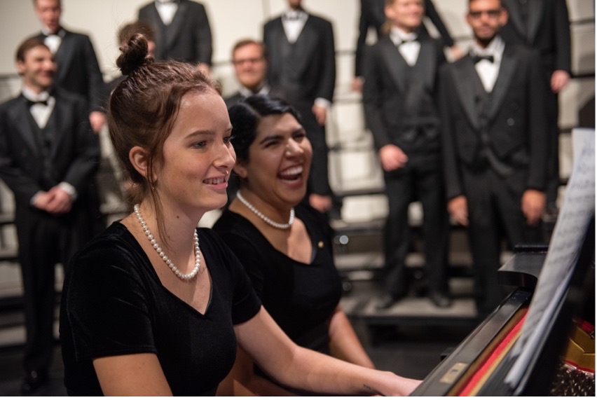 Two students singing at piano on stage.