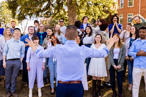 Choir of students singing in front of old main wearing casual clothing