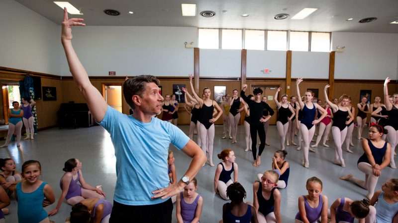 Male dance instructor leading a dance class of both young and older students.