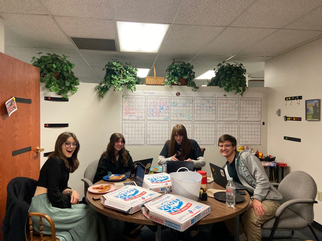 The CAL marketing team enjoying Tuesday Night Dinner at their work session, students, pizza boxes and laptops gathered around a table