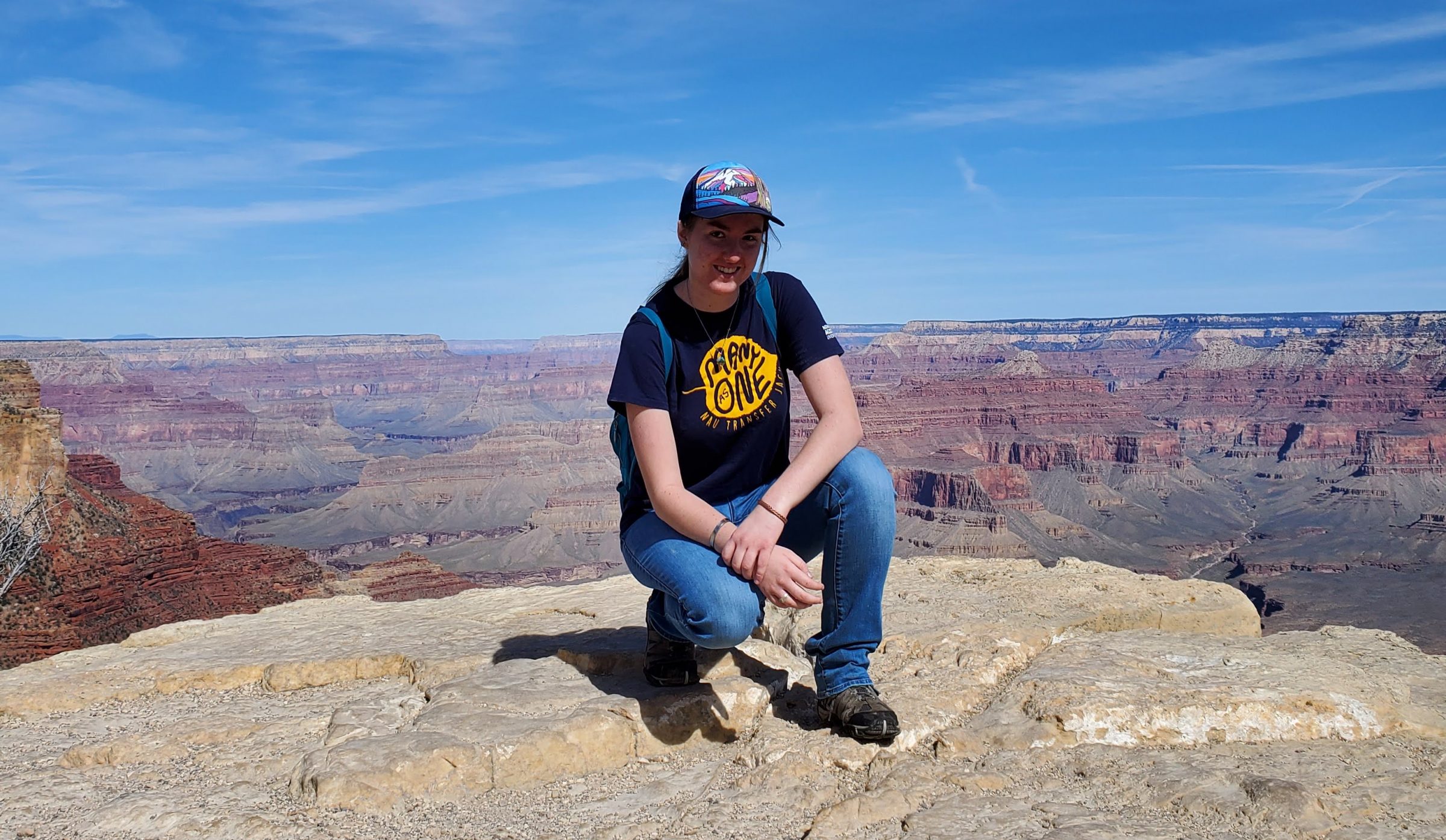 Kaylen Wilson kneeling down and smiling at the edge of the Grand Canyon.