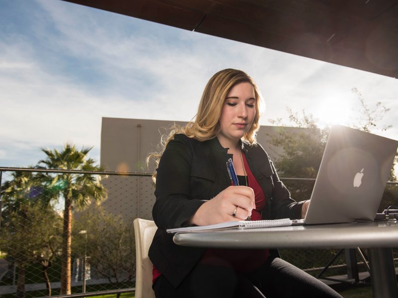 professional adult writing with an open laptop, sitting at a table outside.