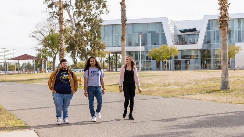 Tres estudiantes caminan juntos afuera y platican en el campus de NAU.